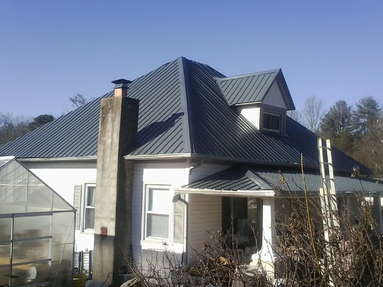 Dark blue standing seam metal roof on a white farmhouse with dormer — Slate & Tile Roof Repair by Roofing Brothers in Hedrick