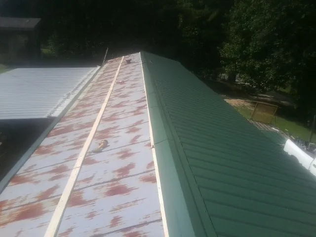Old rusted panels beside newly installed green metal roofing — Wind Damage Roof Repair by Roofing Brothers in Hedrick