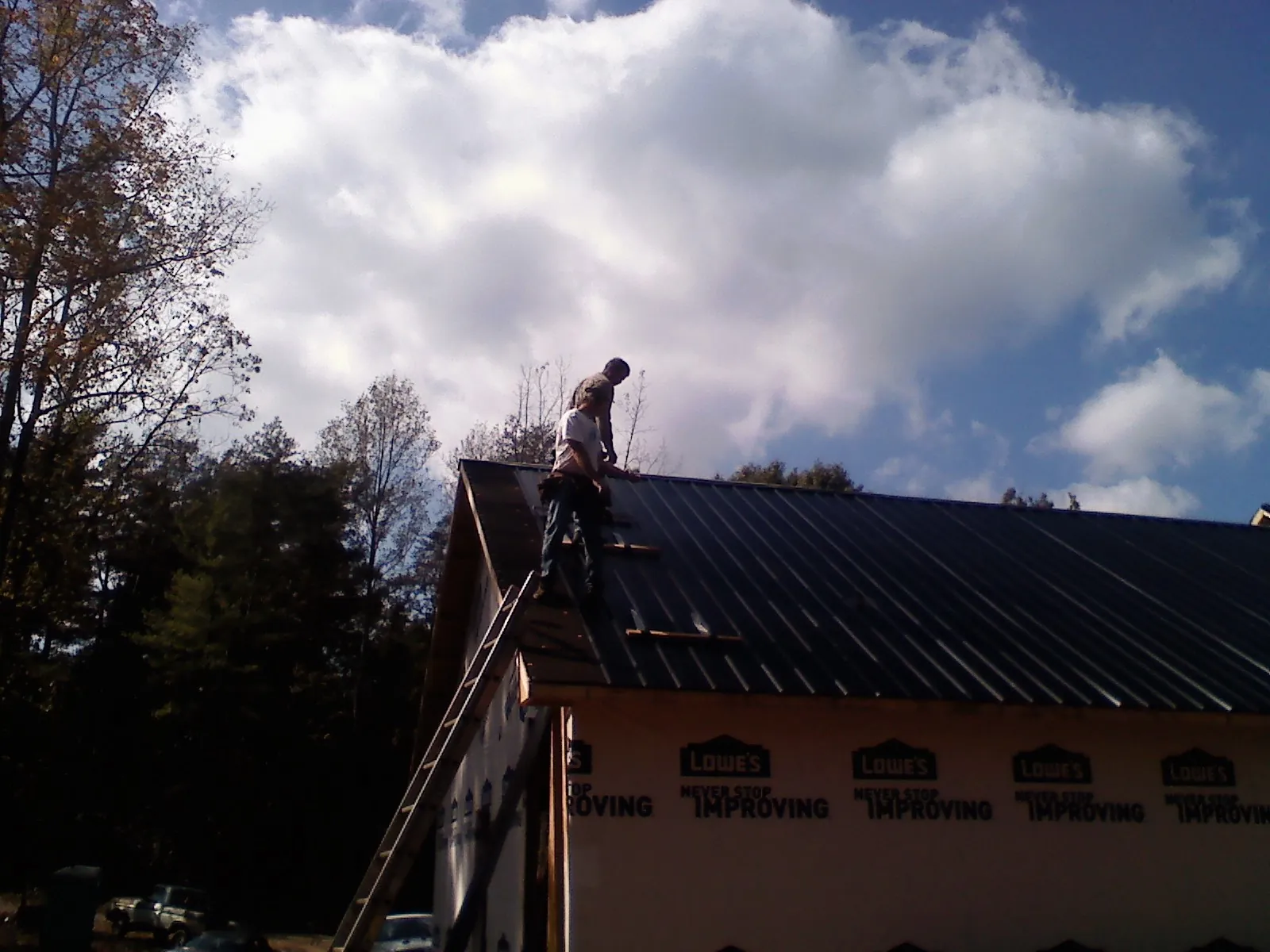 Roofer fastening dark metal panels high against a cloudy sky, from a Roof Inspection job in Hedrick