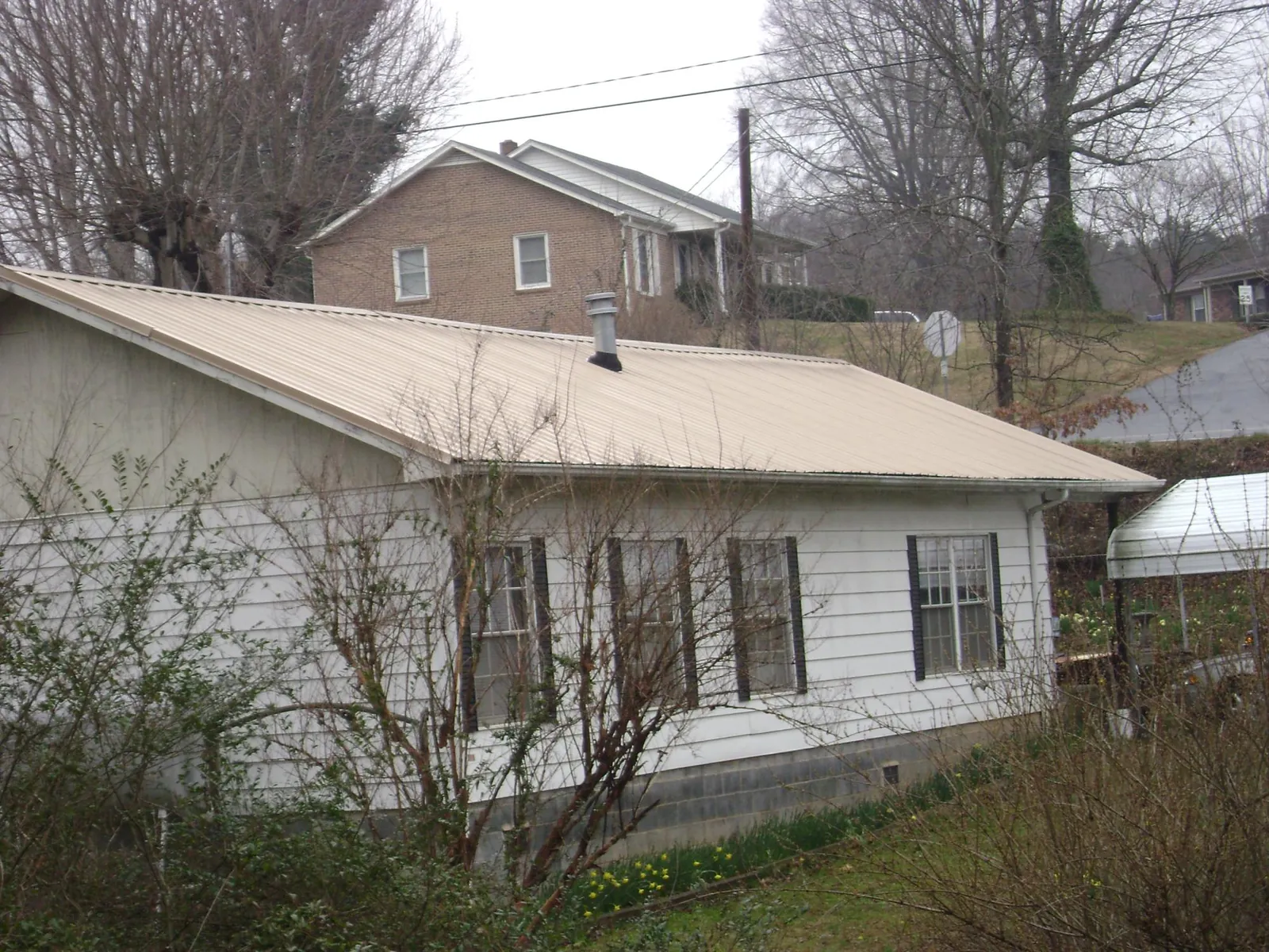 Tan metal roof on a white sided house set into a hillside — Commercial Roofing by Roofing Brothers in Hedrick