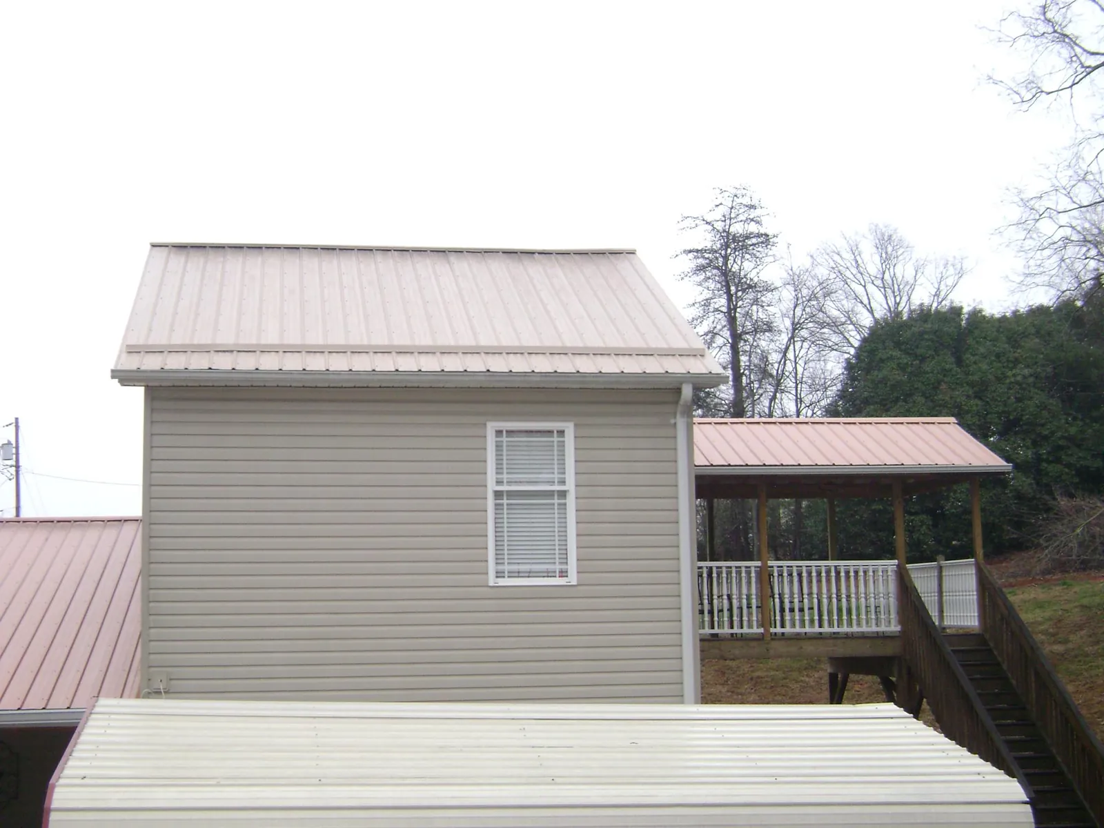 Tan metal roofs on a two story addition and attached porch, from a Roof Replacement job in Hedrick