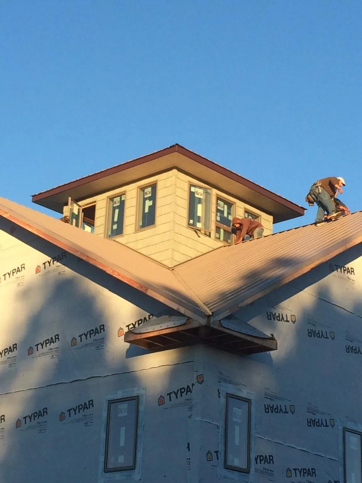 Roofers working around a rooftop cupola on a new metal roof at sunset — Roof Waterproofing in Hedrick by Roofing Brothers